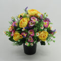 Memorial artificial flowers: yellow roses, purple sprigs, pink blooms in black pot