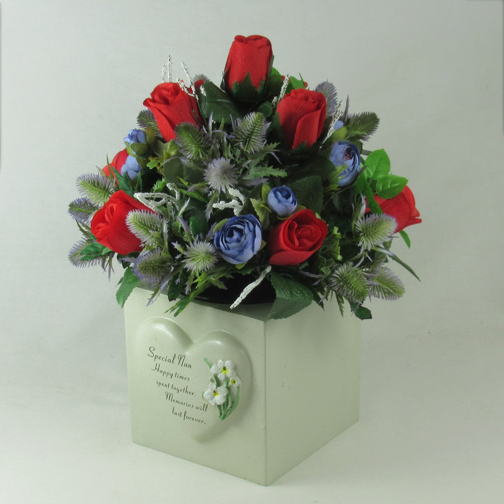 Artificial memorial flower arrangement with red roses and blue blooms in white keepsake box