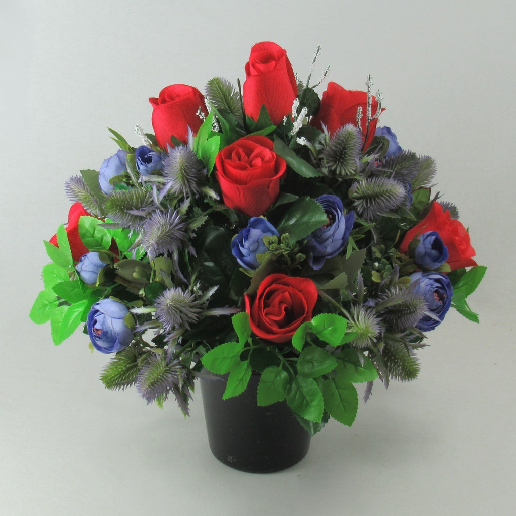 Handmade artificial memorial flowers: red roses, blue blooms, green foliage in black pot