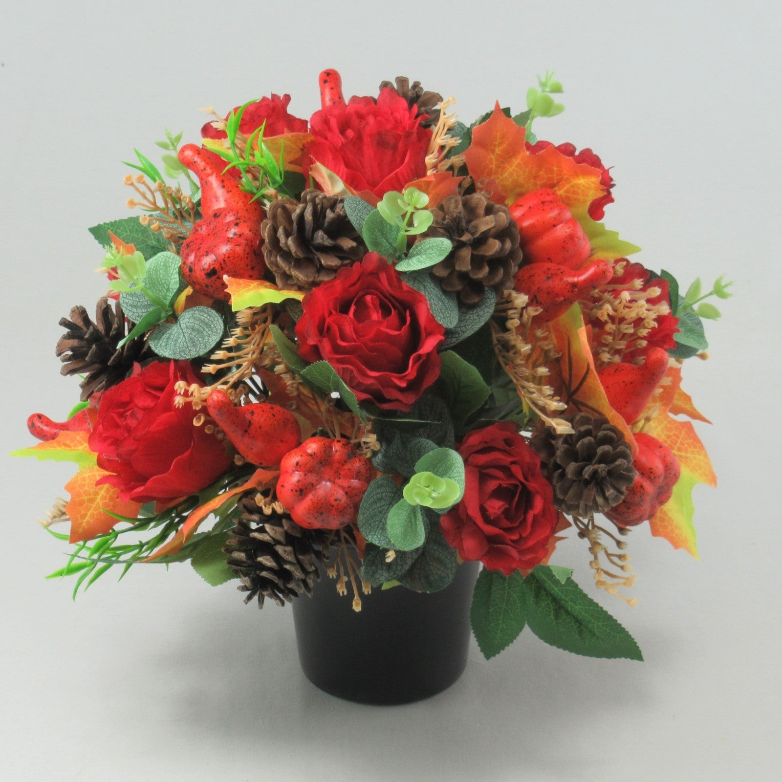 Autumn grave flower arrangement with red roses, pinecones, red berries, and fall leaves in pot