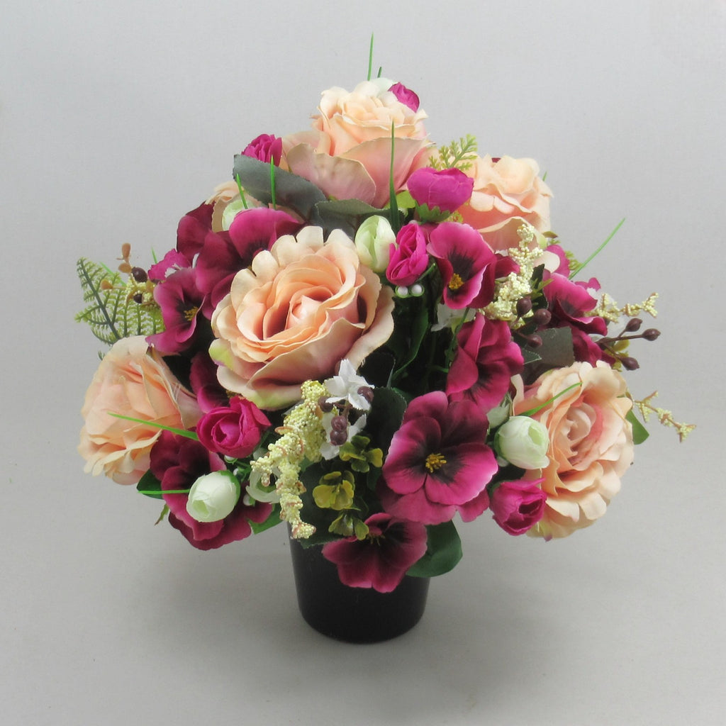 Artificial memorial bouquet in black pot: peach roses, purple flowers, green leaves