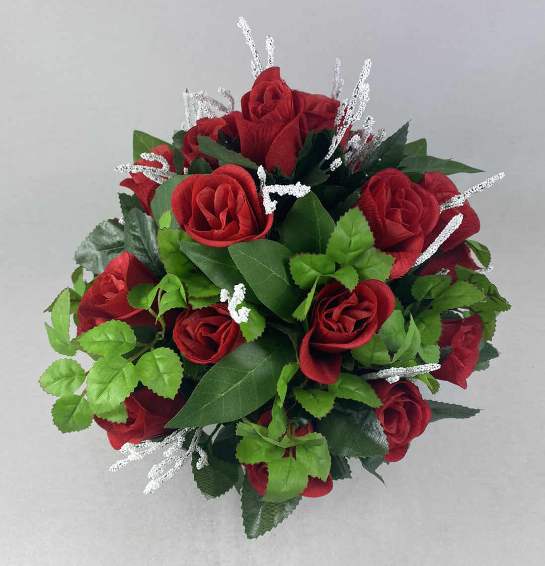 Close view of large artificial arrangement with red roses, green leaves, and silver twig sprays.