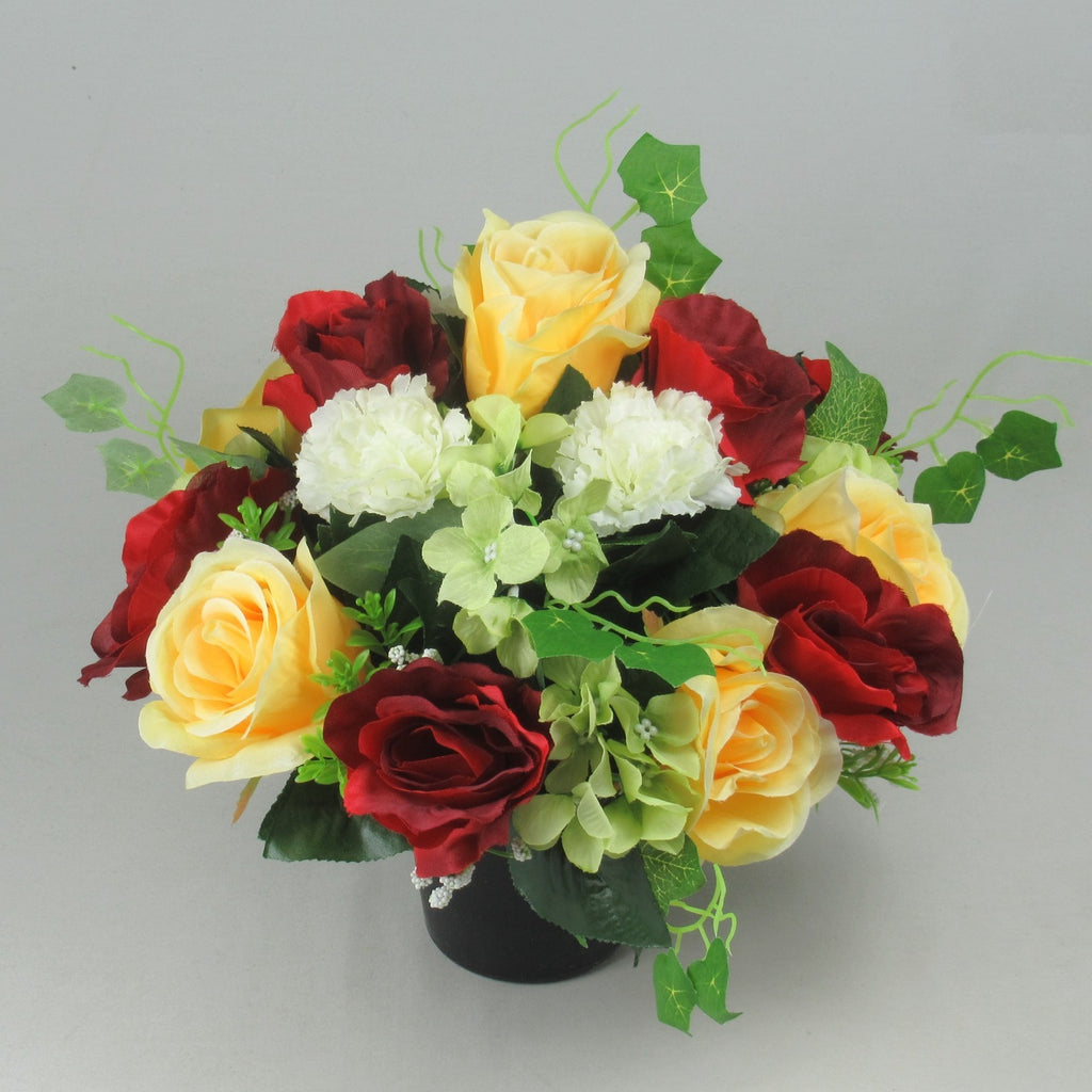 Artificial grave arrangement in black vase with yellow roses, red roses, and white hydrangea
