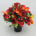 Artificial autumn grave arrangement in black pot with red roses, orange/yellow leaves, red berries