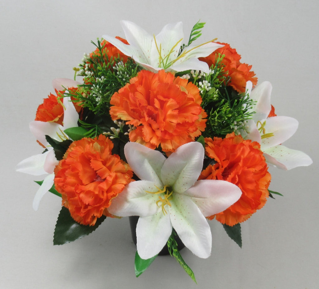 Orange carnation-style blooms and white lilies with green sprigs in black pot arrangement