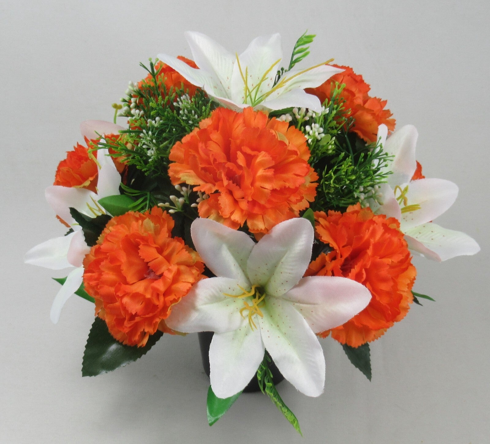 Orange carnation-style blooms and white lilies with green sprigs in black pot arrangement