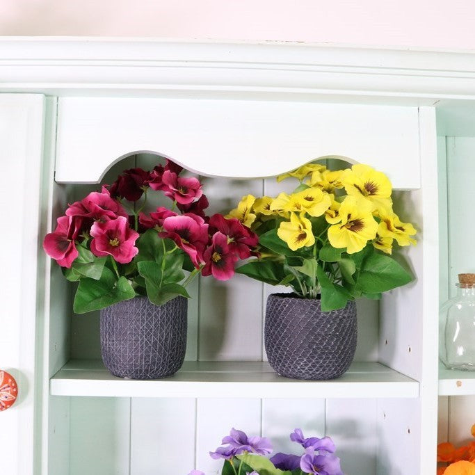 Artificial silk pansy bunch with magenta, yellow, and purple blossoms and green leaves