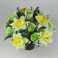 Green rose and yellow daffodil artificial flowers in dark pot, white sparkly stems, purple sprigs