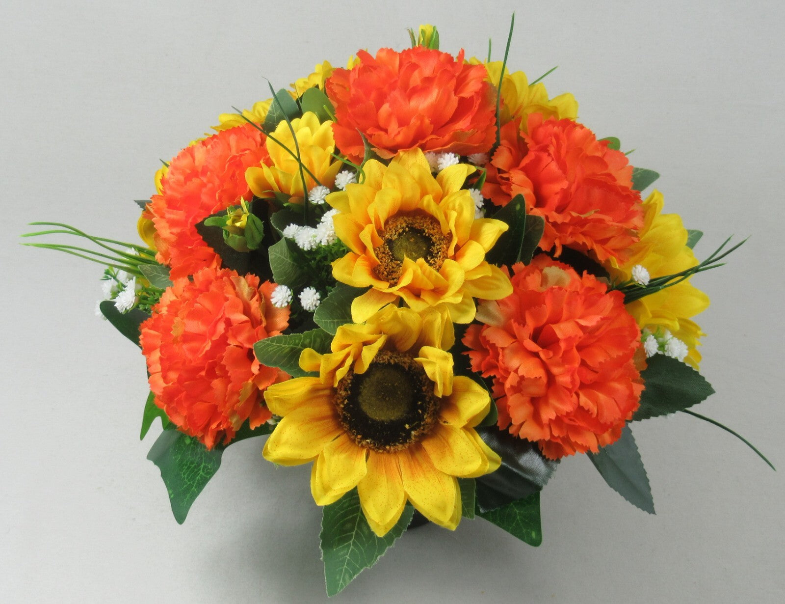 Artificial grave arrangement in dark pot with orange carnations, yellow sunflowers, and green leaves