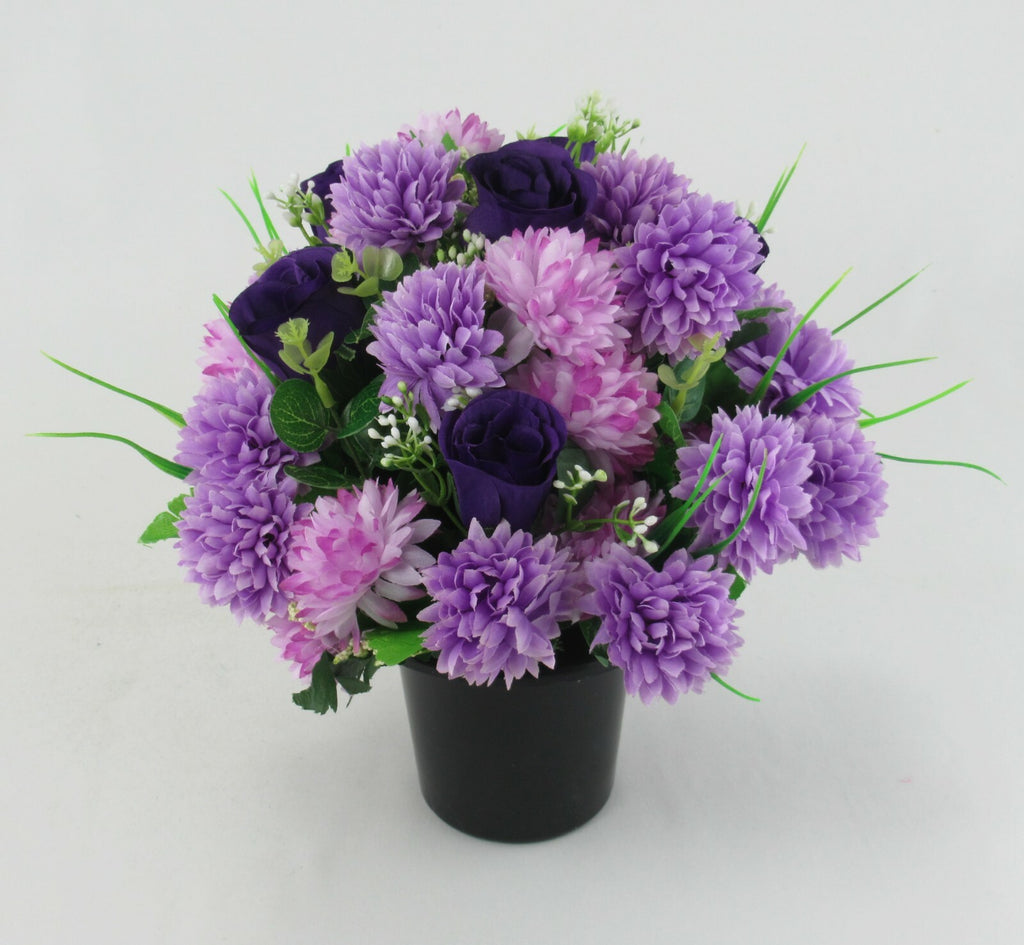 Purple artificial flower memorial pot with dark navy roses, green leaves and small white buds