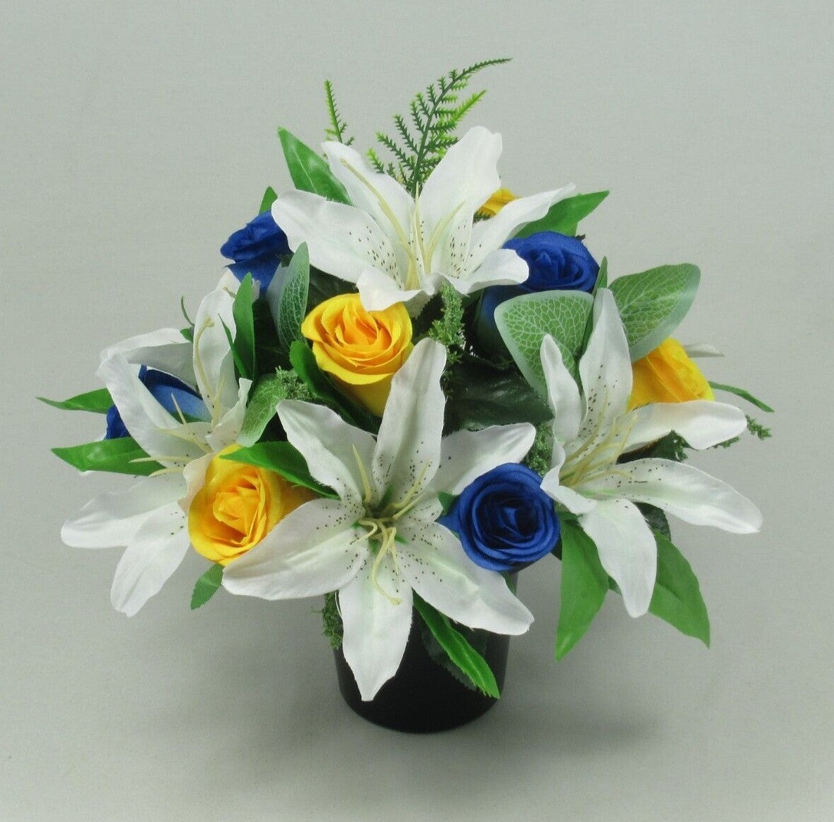 Artificial silk grave pot centerpiece with white lilies, blue roses, yellow roses, green greenery
