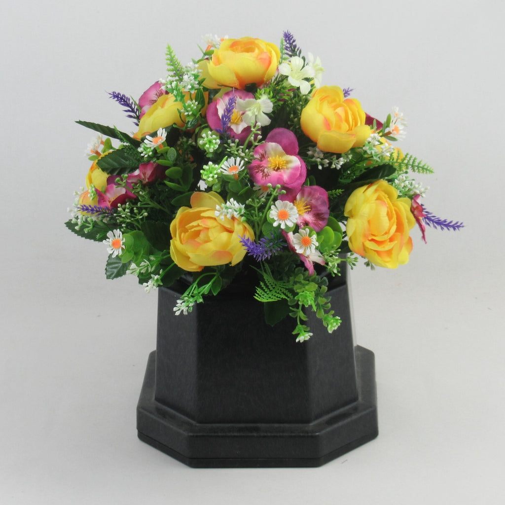 Artificial memorial flowers on black planter with yellow roses, purple sprigs, pink blooms, daisies