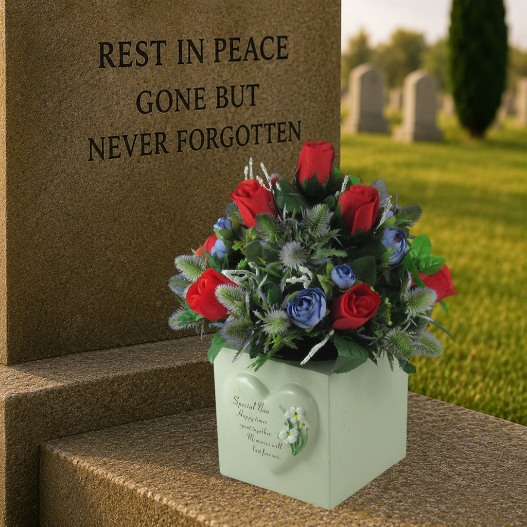 Artificial memorial bouquet with red roses, blue flowers, and green foliage in white box