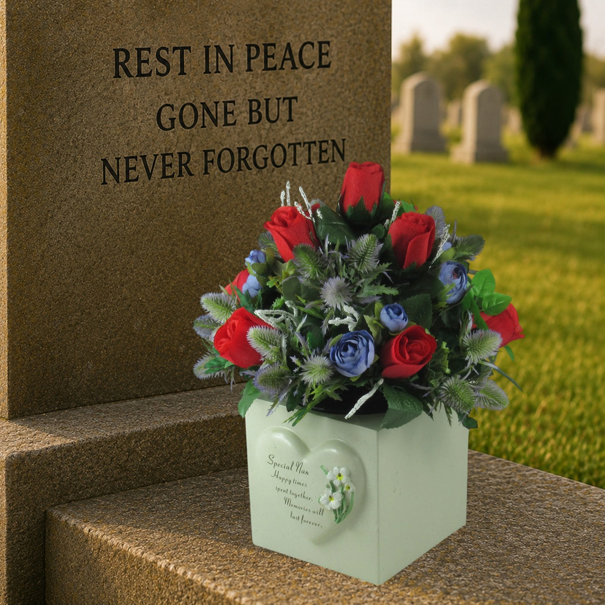 Artificial memorial bouquet with red roses, blue flowers, and green foliage in white box