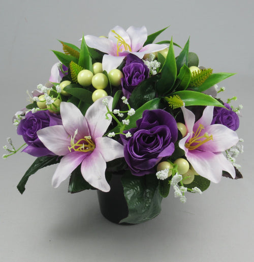 Purple rose and lilac lily grave flower arrangement in dark pot with green leaves