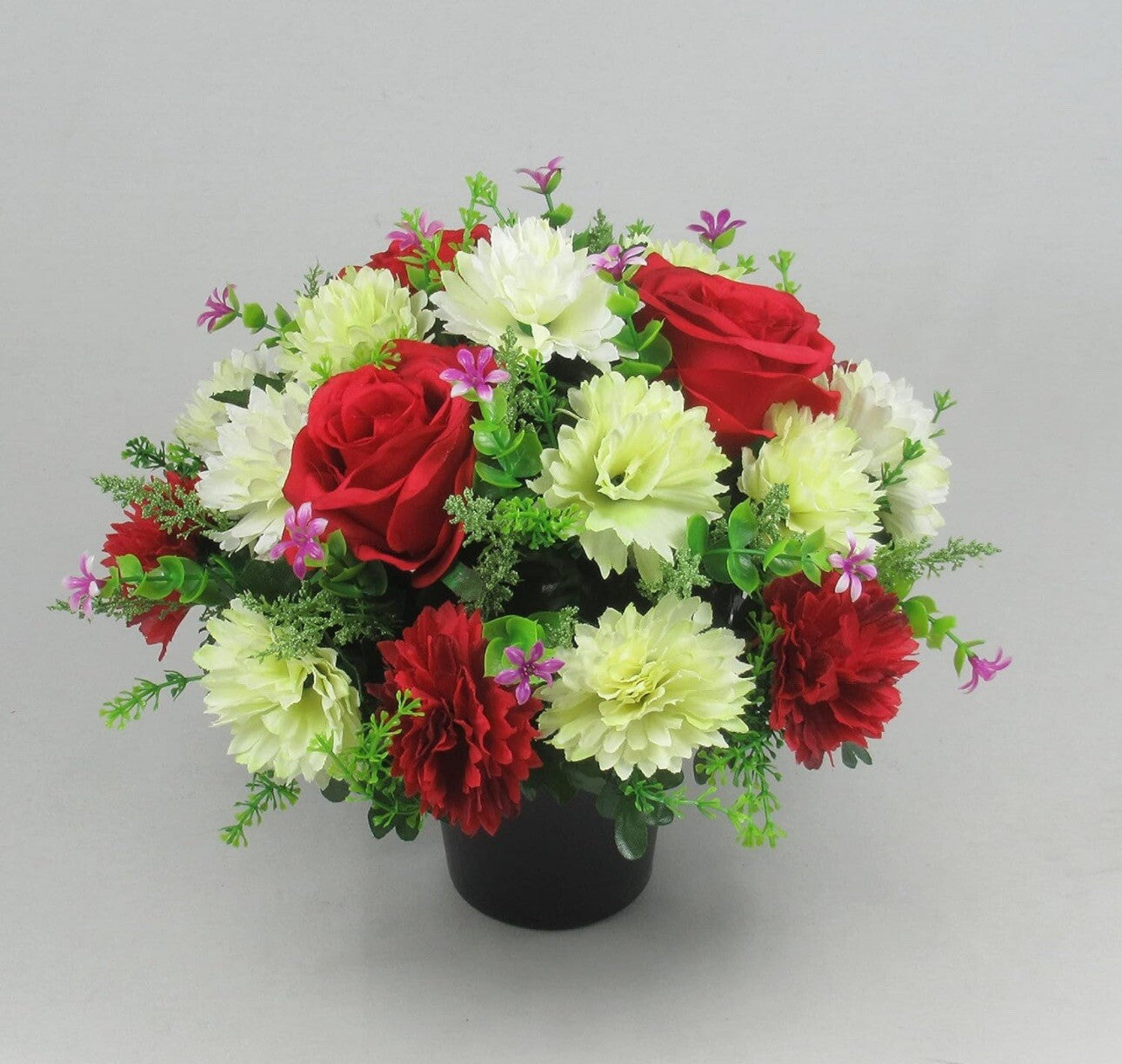 Artificial grave crem pot arrangement with red and white flowers, purple sprigs in black pot