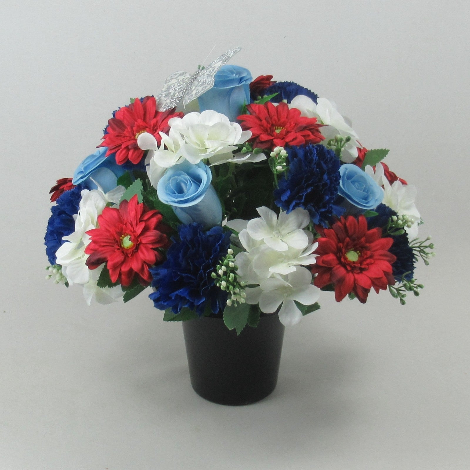 Artificial grave flower arrangement in black pot with blue rose-like blooms, red and white flowers.