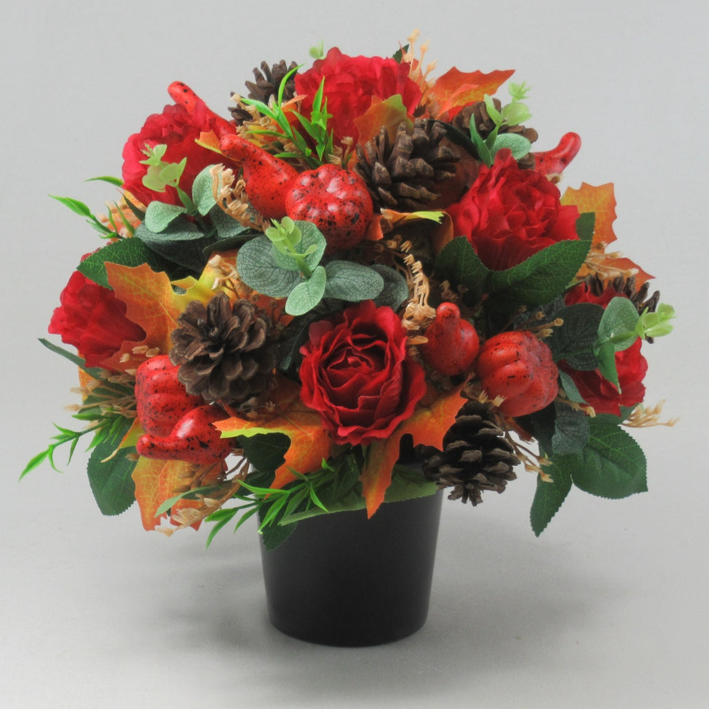 Front view of warm autumn grave flowers with red roses, pinecones, red berries, and orange leaves