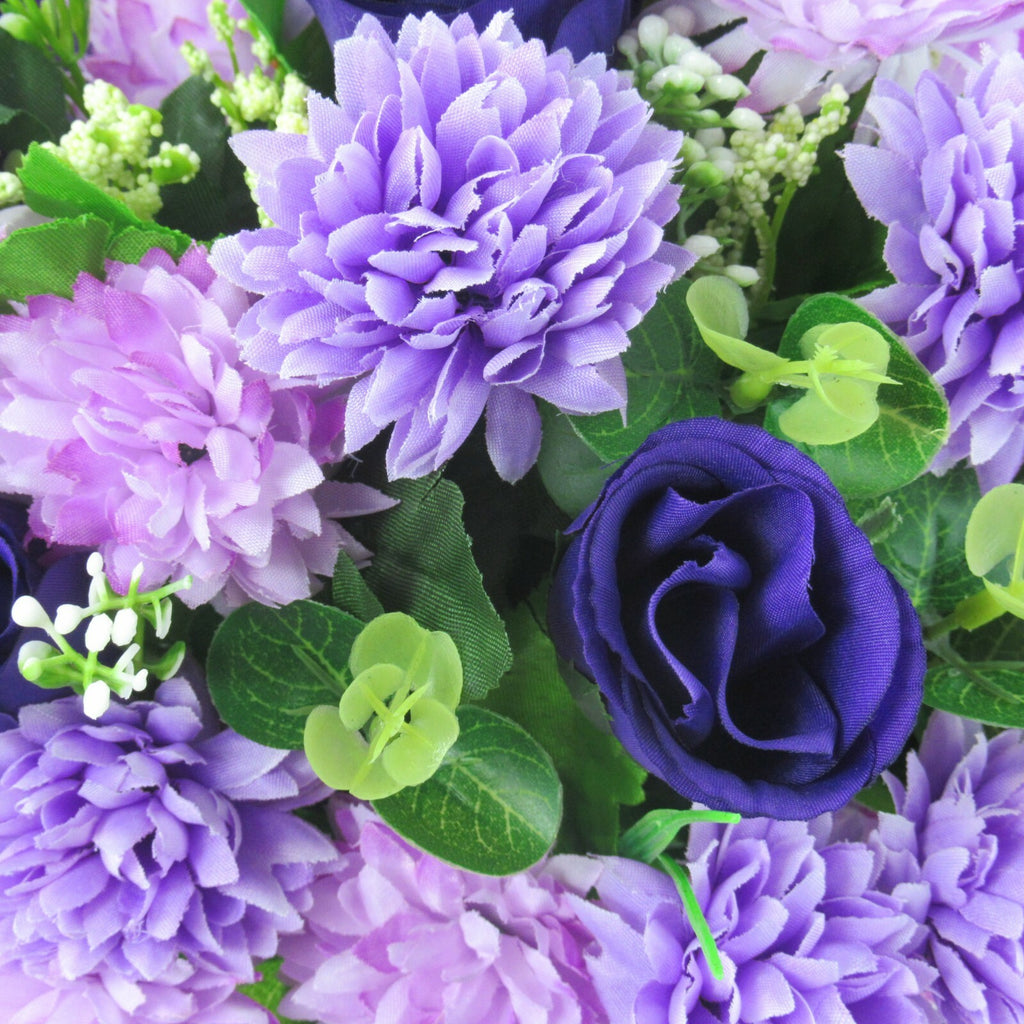 Close-up of purple artificial flowers with dark navy rose and green leaves in memorial pot