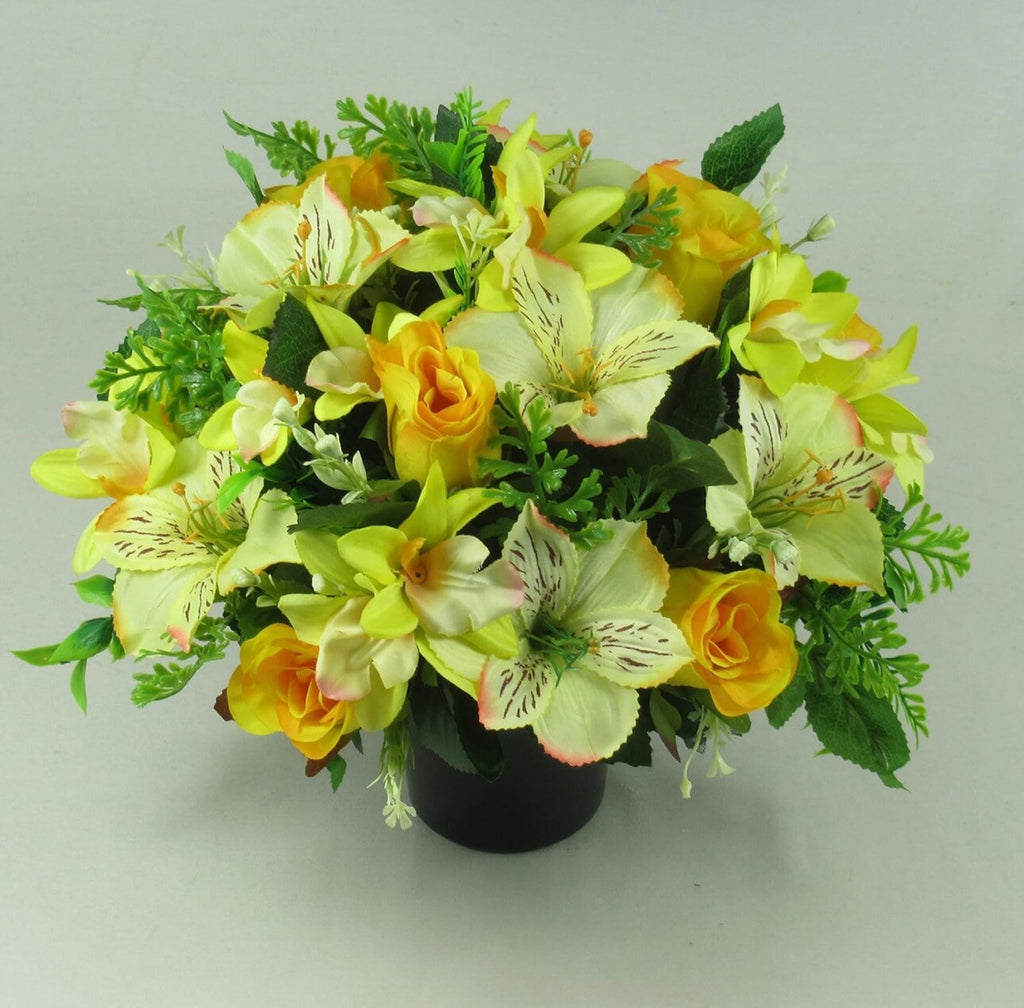 Yellow, white, and orange faux flowers in black memorial pot with leafy foliage