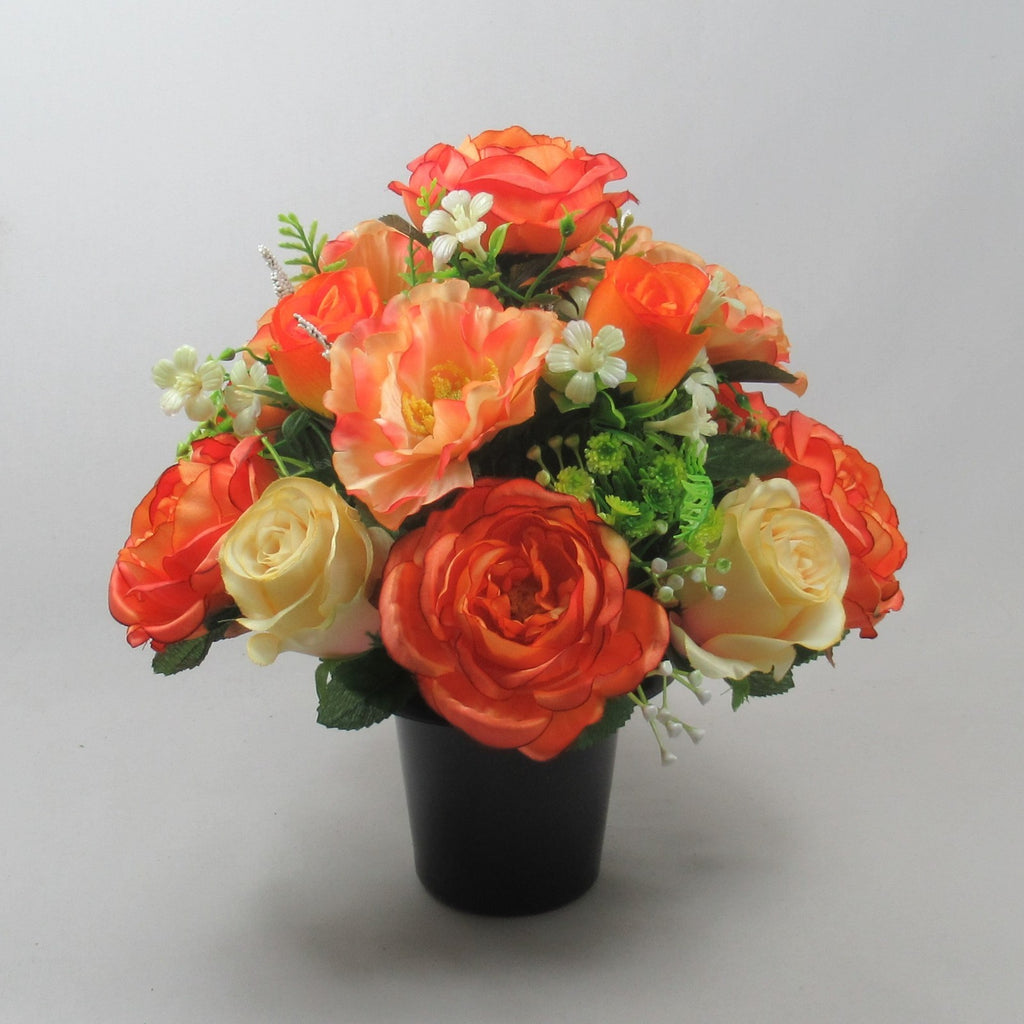 Artificial rose bouquet in black vase with orange, red, and cream flowers and green leaves