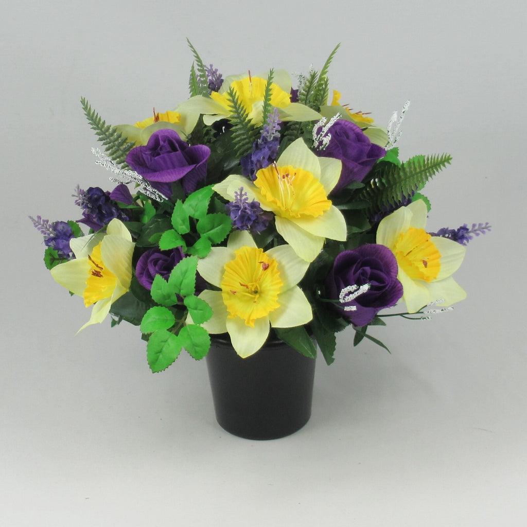 Memorial grave pot with yellow daffodil-style blooms, purple roses, green leaves—artificial