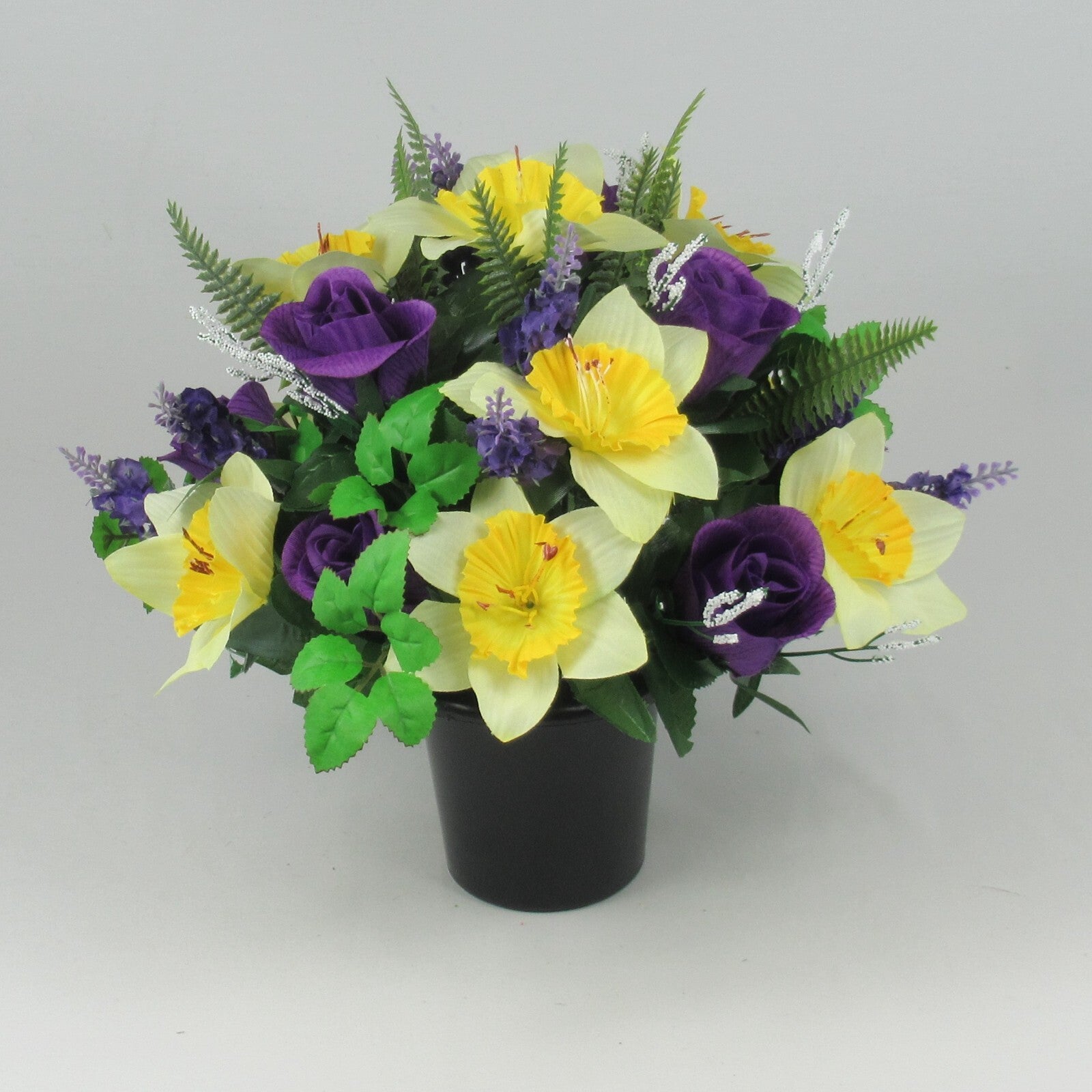 Memorial grave pot with yellow daffodil-style blooms, purple roses, green leaves—artificial