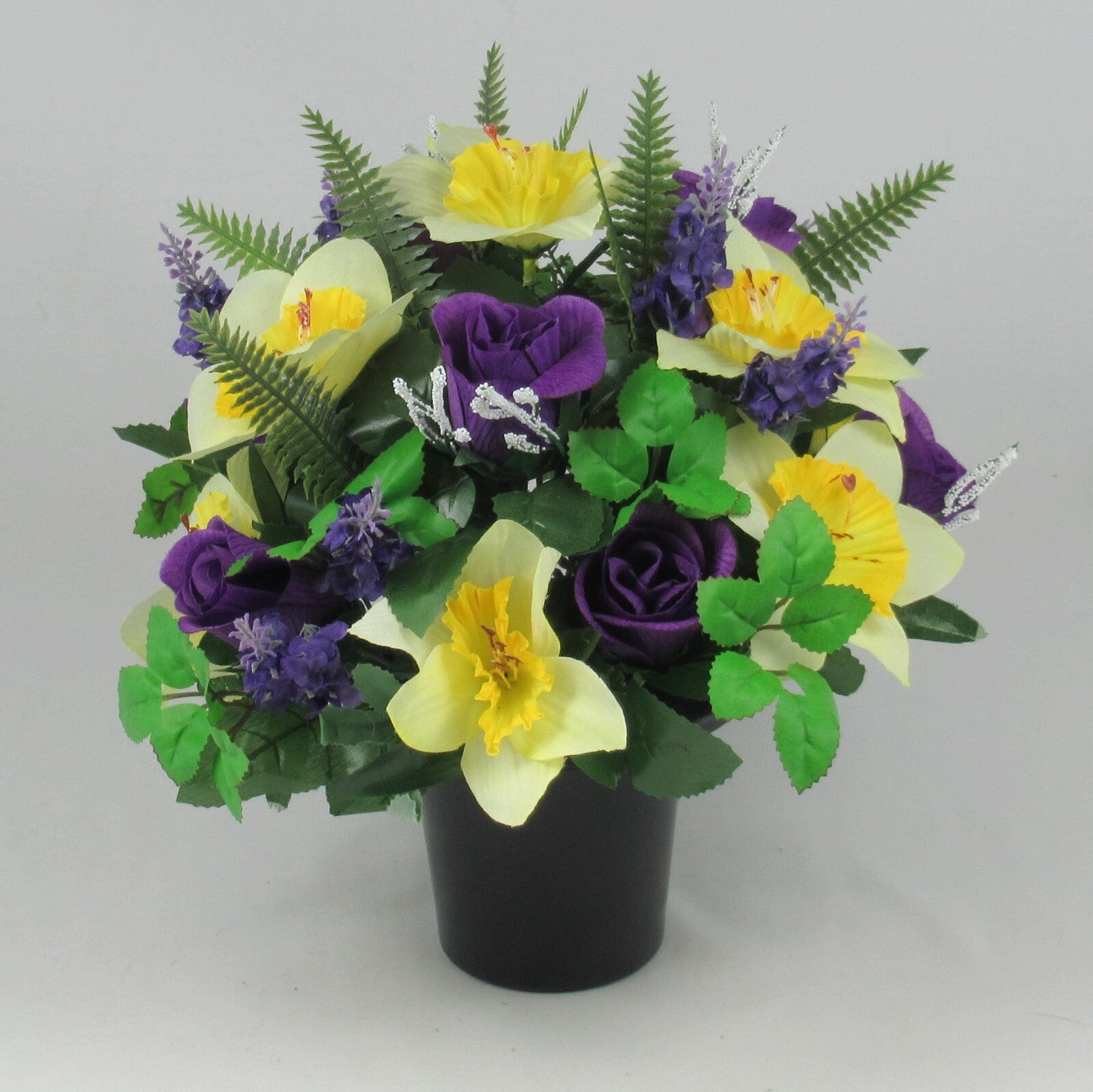 Round memorial grave pot centerpiece with yellow daffodils, purple roses, lavender sprigs—artificial