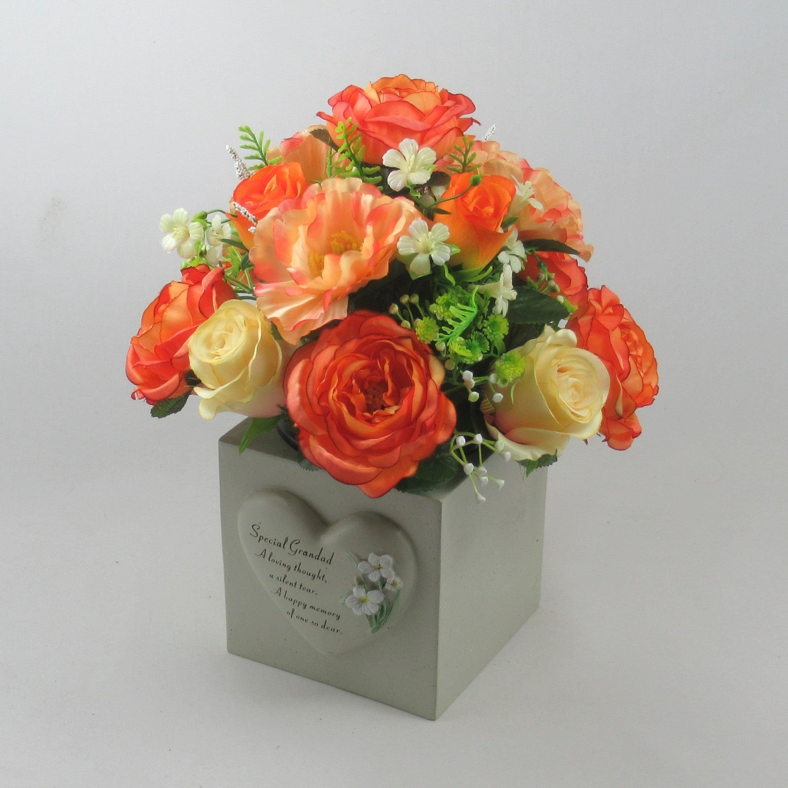 Artificial rose arrangement in black pot on a gray memorial-style base with printed wording