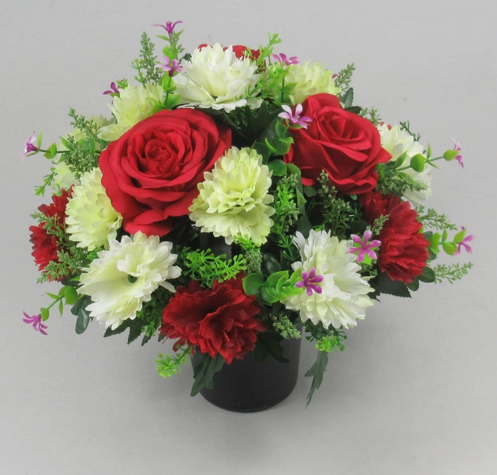 Artificial bouquet in black crem pot with two red roses, white flowers, purple accents and greenery