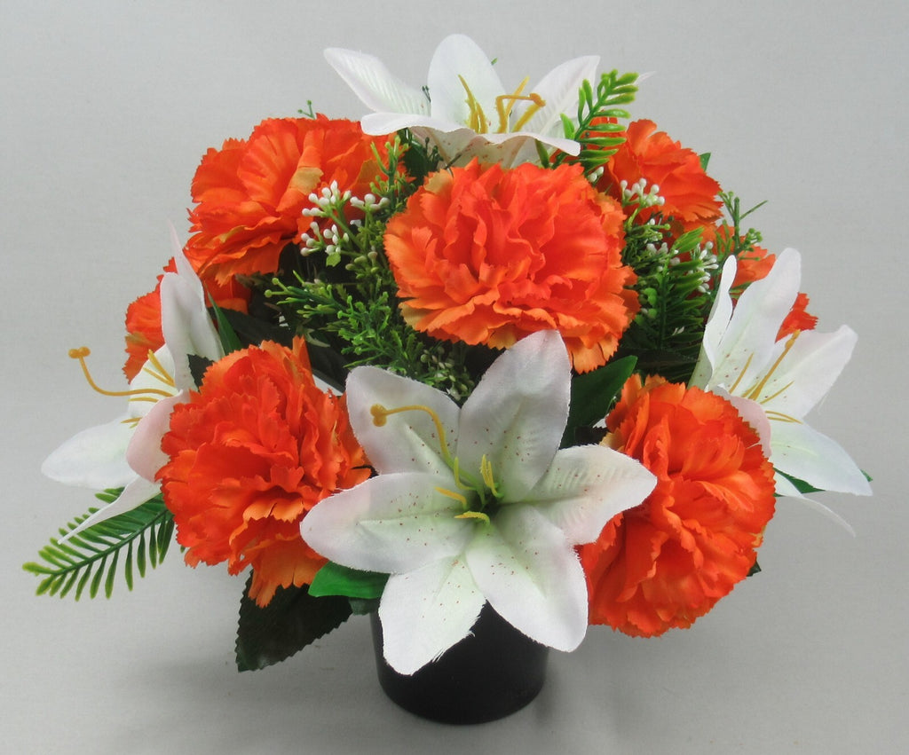 Top view of orange carnation-style flowers with white lilies and greenery in black pot