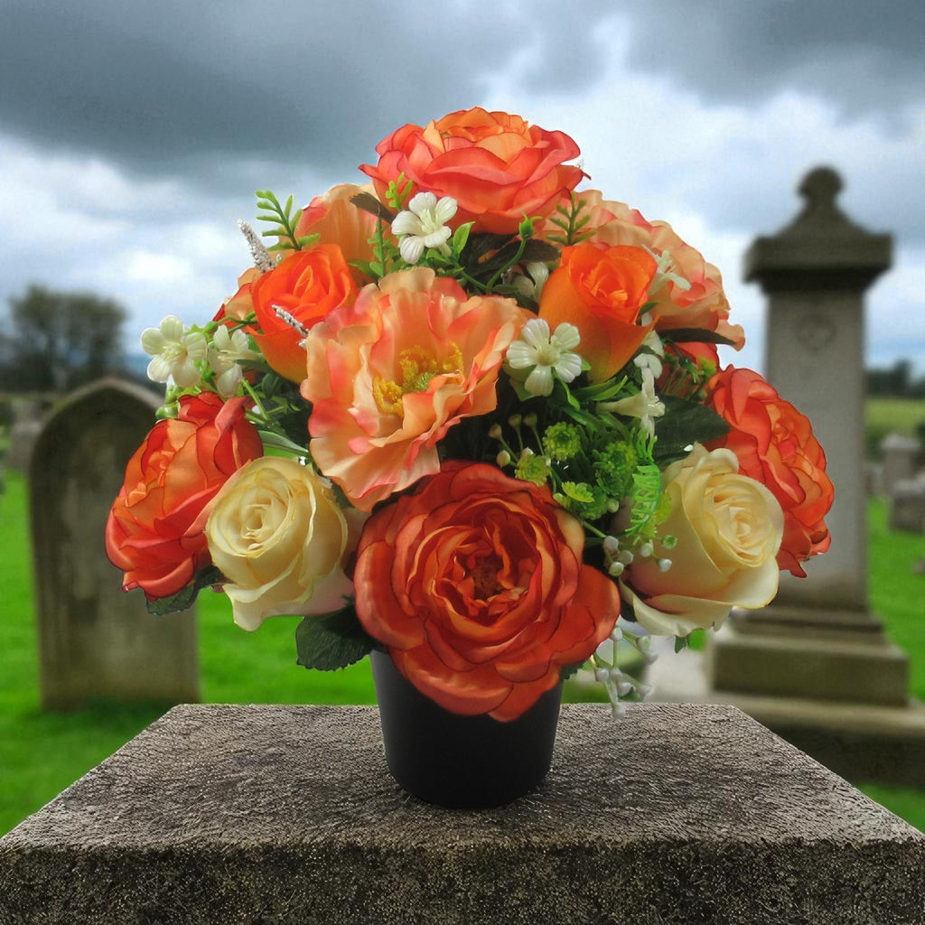 Artificial autumn flower arrangement in black pot with orange red and cream roses, outdoor view