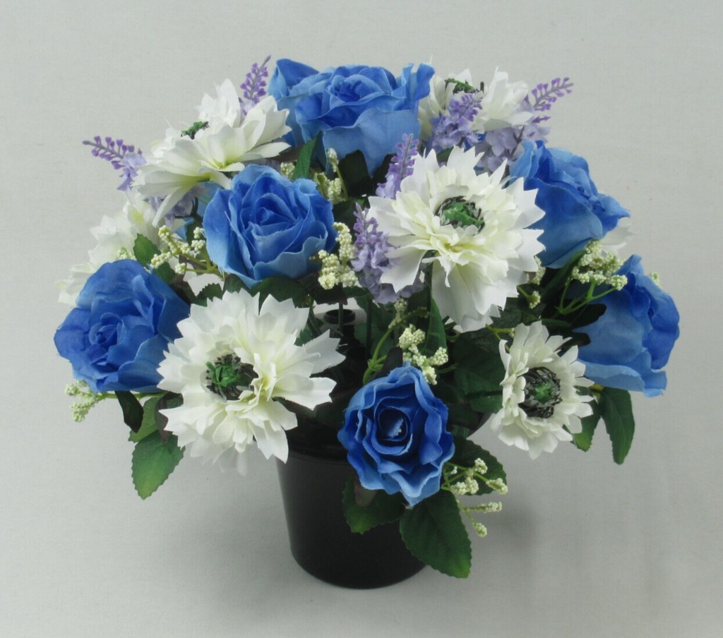 Overhead-leaning view of artificial memorial grave pot flowers: blue roses, white blooms, purple sprigs