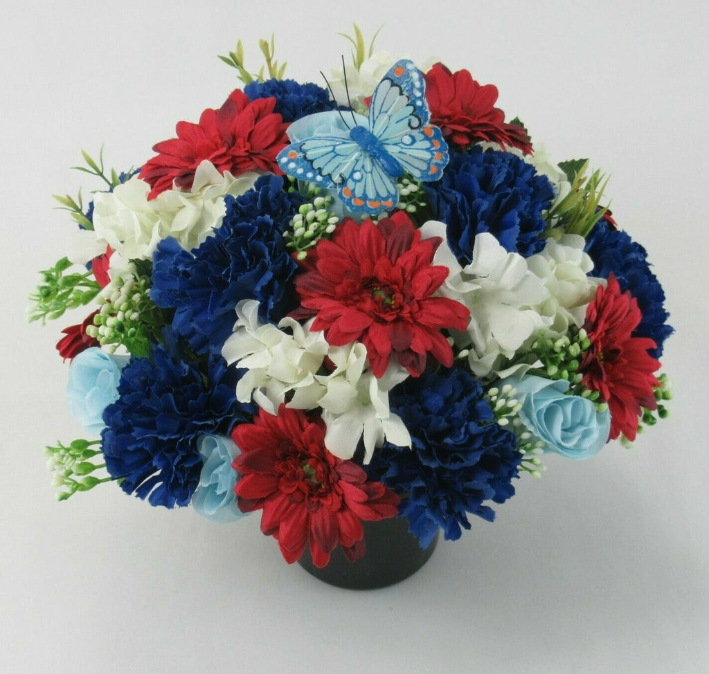 Memorial grave flower arrangement in dark pot with red, blue, white blooms and butterfly topper