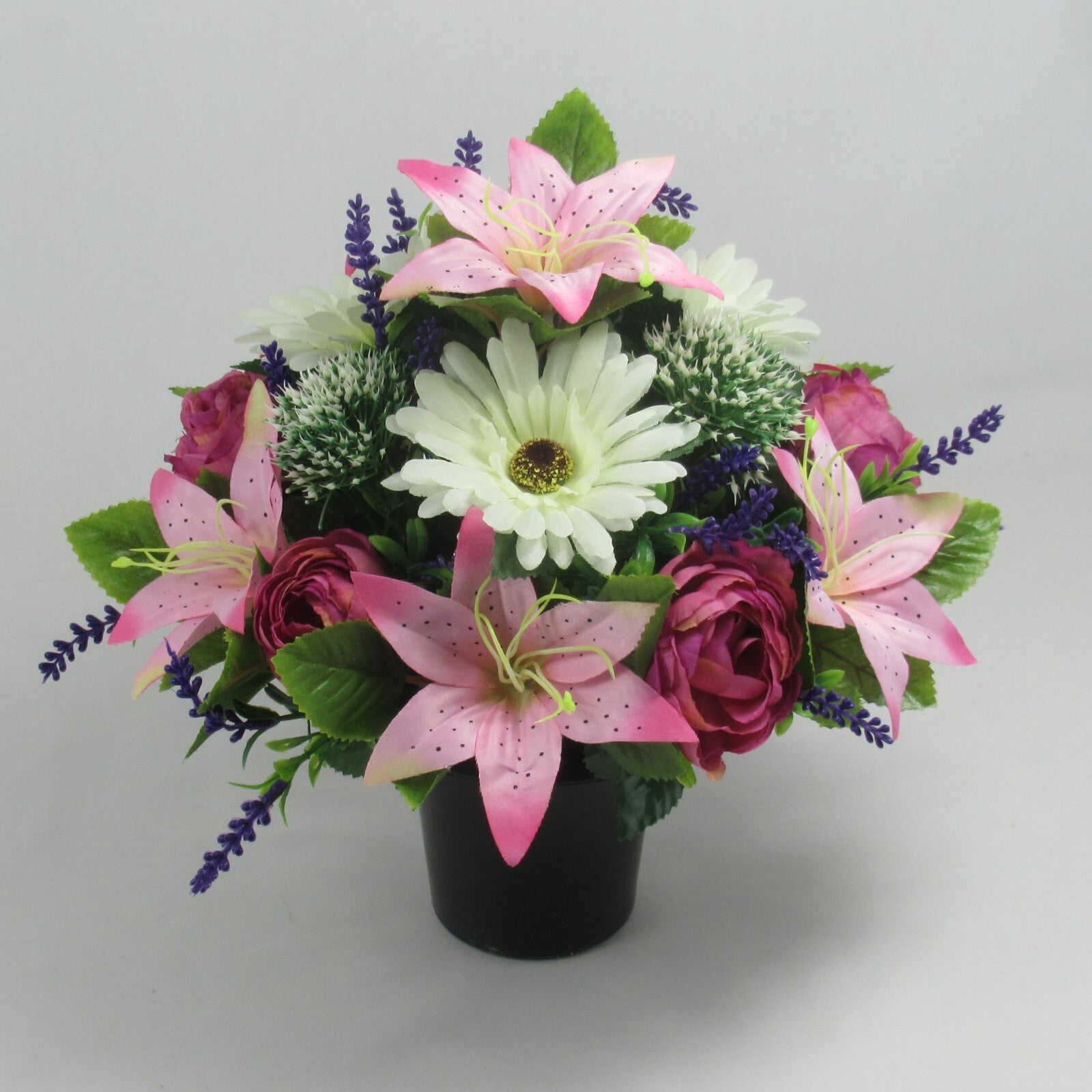 Memorial grave artificial arrangement with pink lilies, white blooms, roses in black pot.