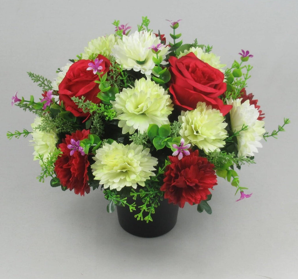 Artificial grave flower arrangement with red roses, pale white dahlias, purple buds, black pot