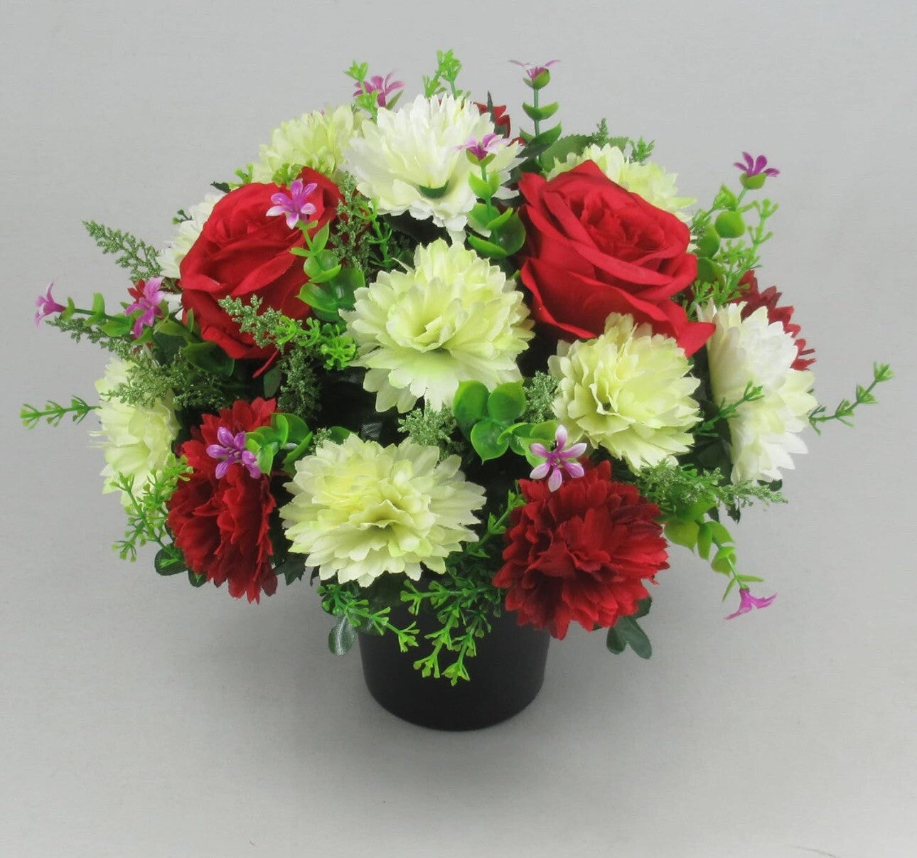Artificial grave flower arrangement with red roses, pale white dahlias, purple buds, black pot