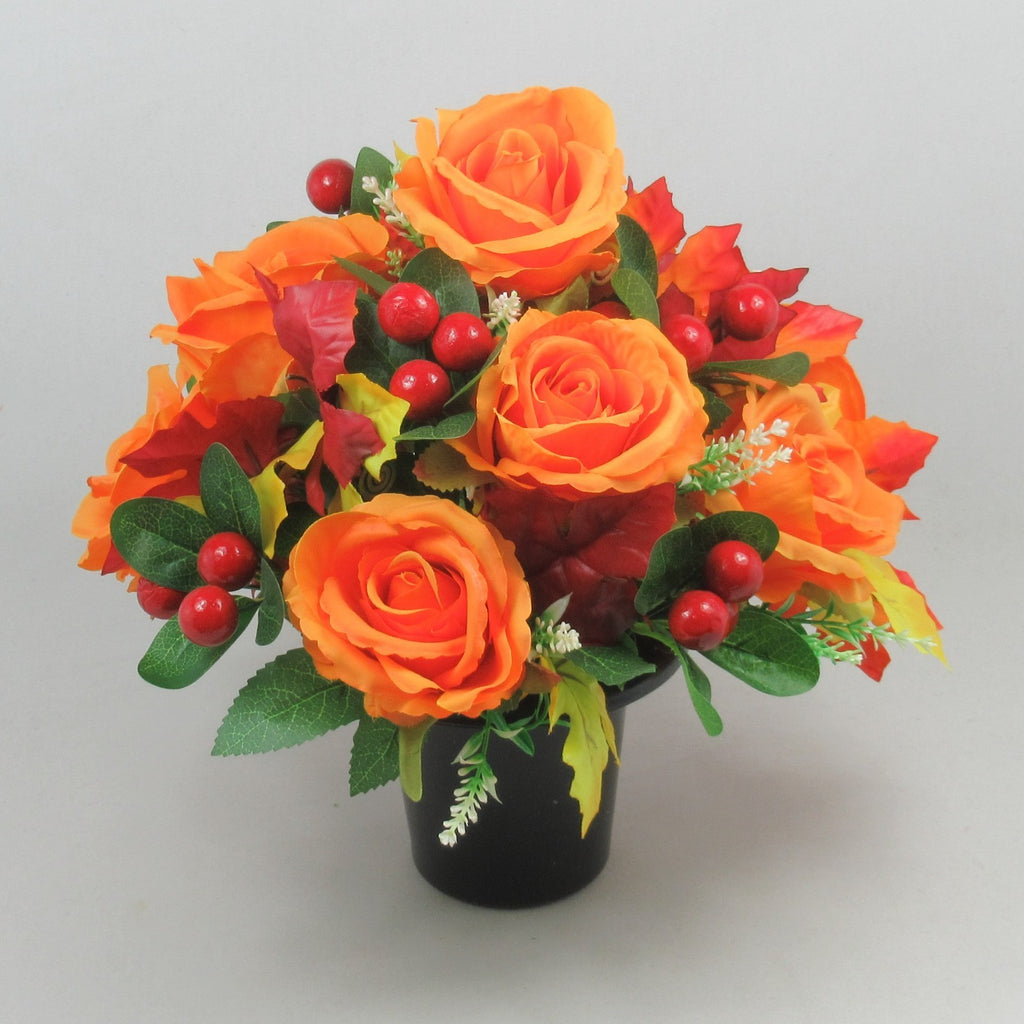 Orange artificial rose memorial grave arrangement in black pot with red berries and green leaves