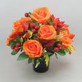 Orange artificial rose memorial grave arrangement in black pot with red berries and green leaves