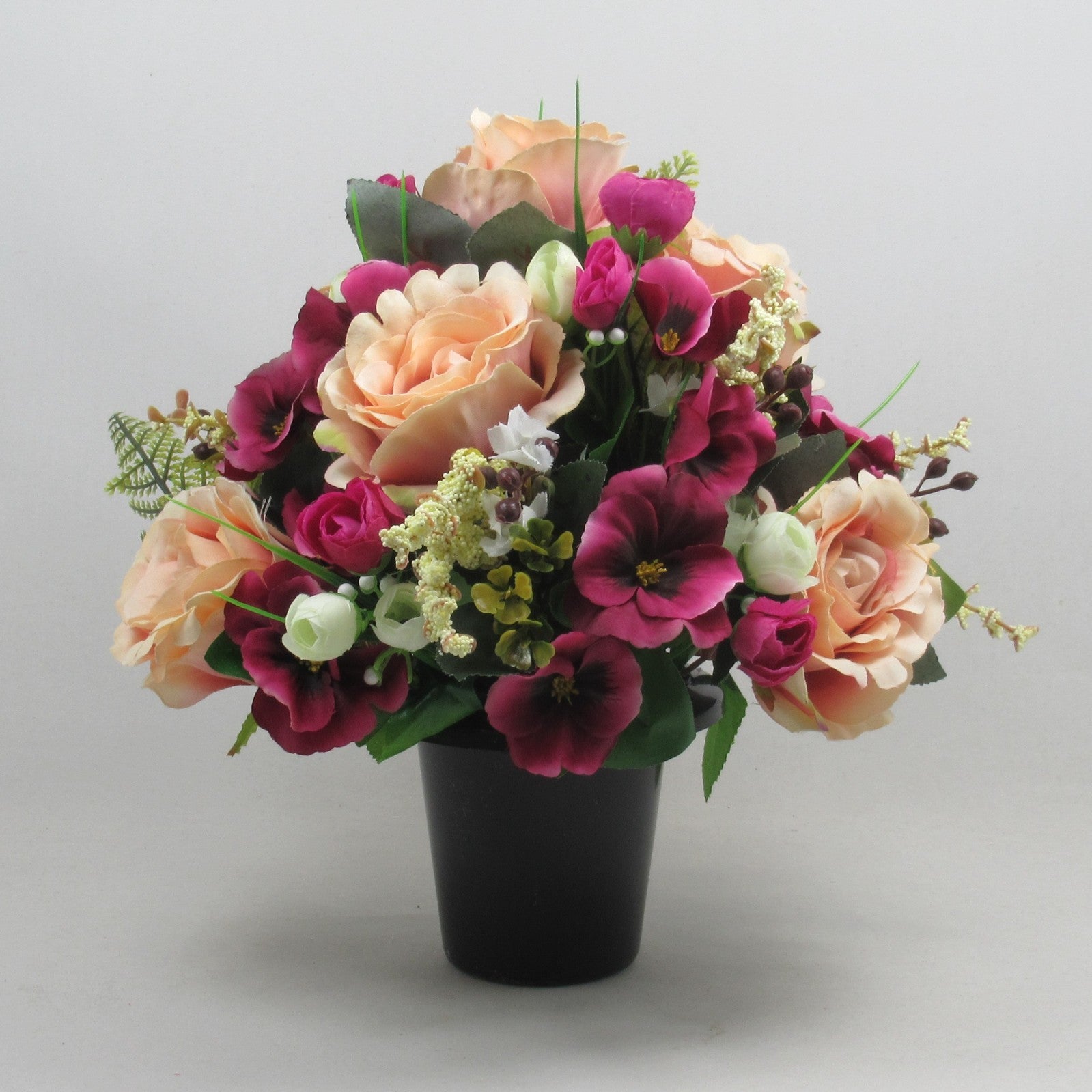 Artificial memorial bouquet in black pot with peach roses and deep magenta flowers