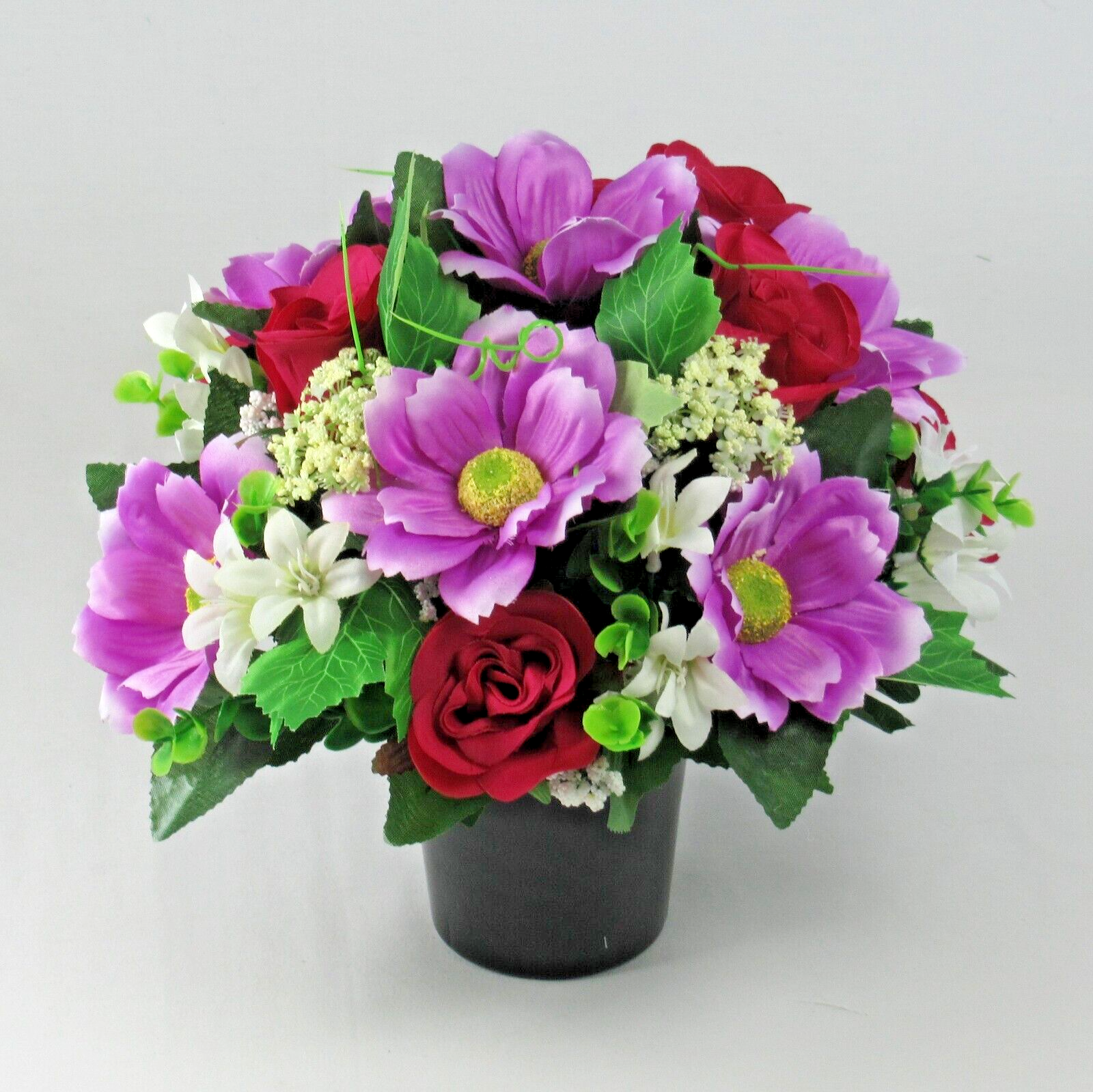 Top view: purple blooms, red roses, and green leaves in black memorial pot