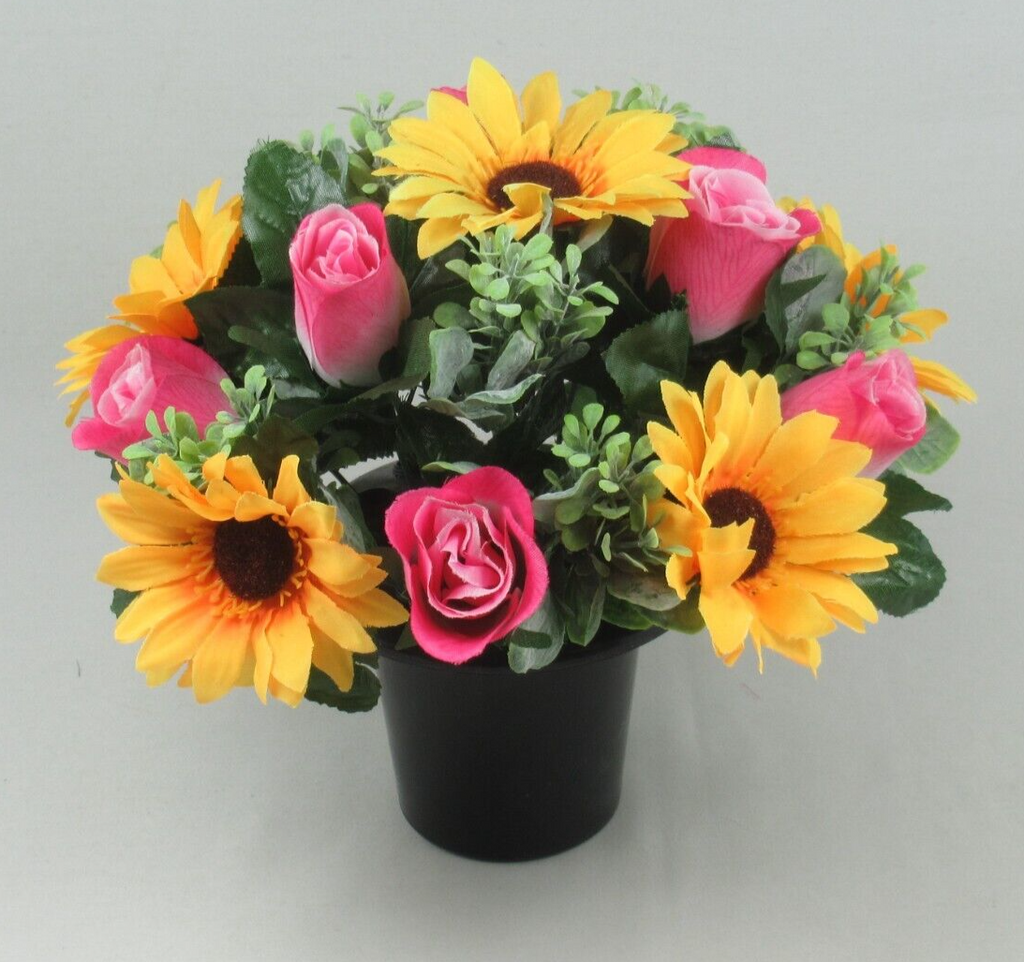 Close view of memorial crem pot: artificial yellow sunflowers and pink roses with green foliage