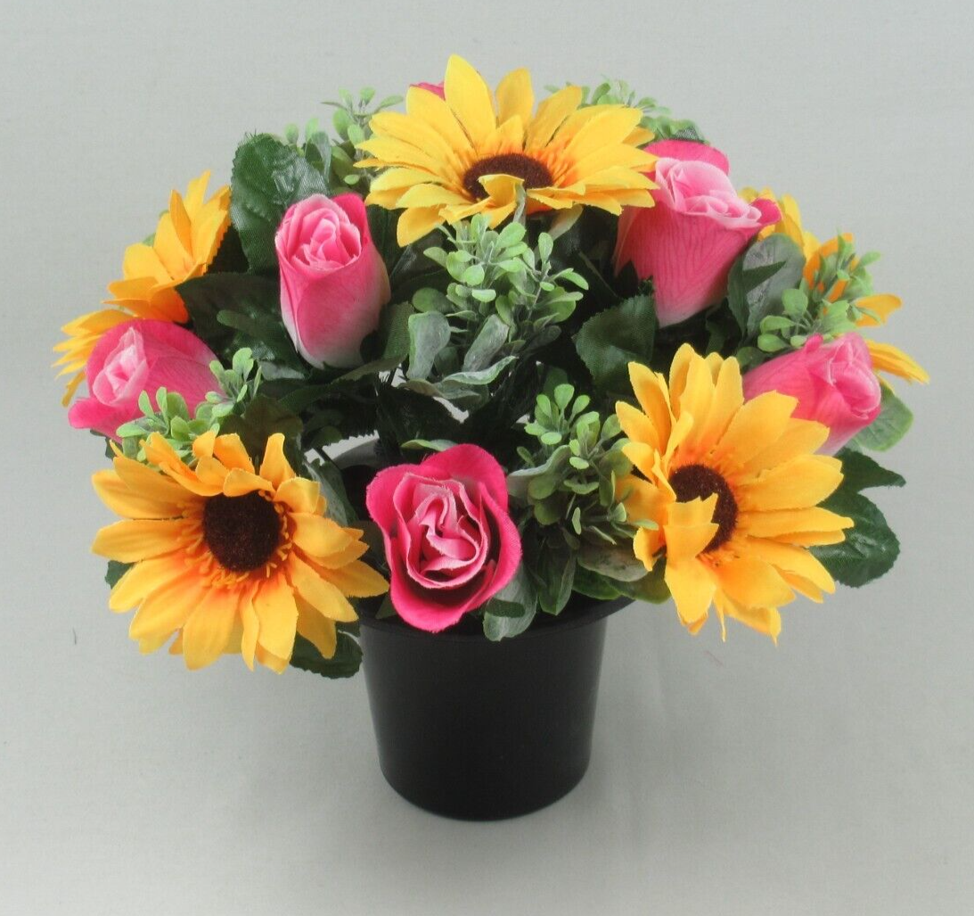 Close view of memorial crem pot: artificial yellow sunflowers and pink roses with green foliage