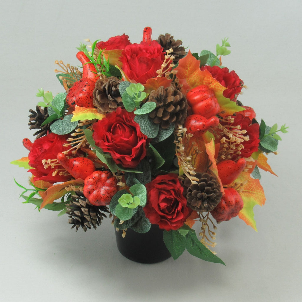 Red rose autumn grave arrangement featuring pinecones, red speckled berries, and orange fall leaves