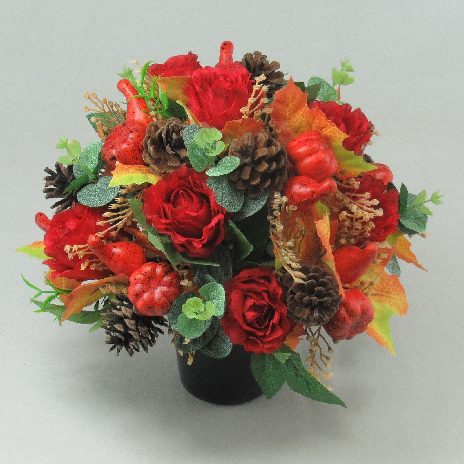 Red rose autumn grave arrangement featuring pinecones, red speckled berries, and orange fall leaves