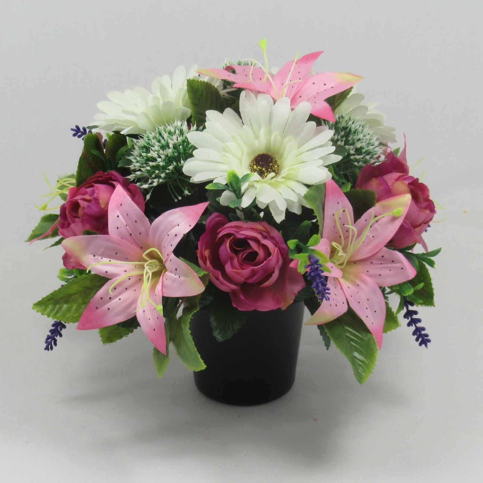 Memorial grave artificial arrangement: white daisy-like blooms, pink lilies, roses, in black pot.