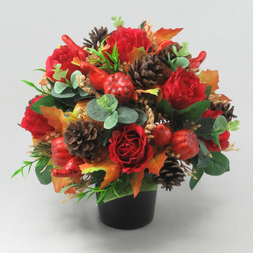 Side view of autumn grave arrangement: red roses, pinecones, speckled berries, and fall leaves in pot