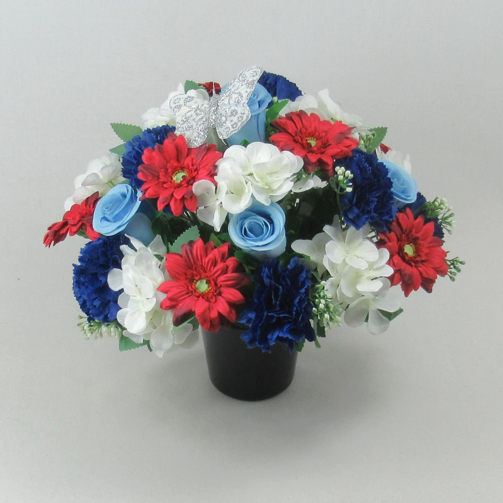 Artificial grave flower arrangement in black pot with red, white, blue blossoms and greenery.