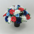 Artificial grave flower arrangement in black pot with red, white, blue blossoms and greenery.