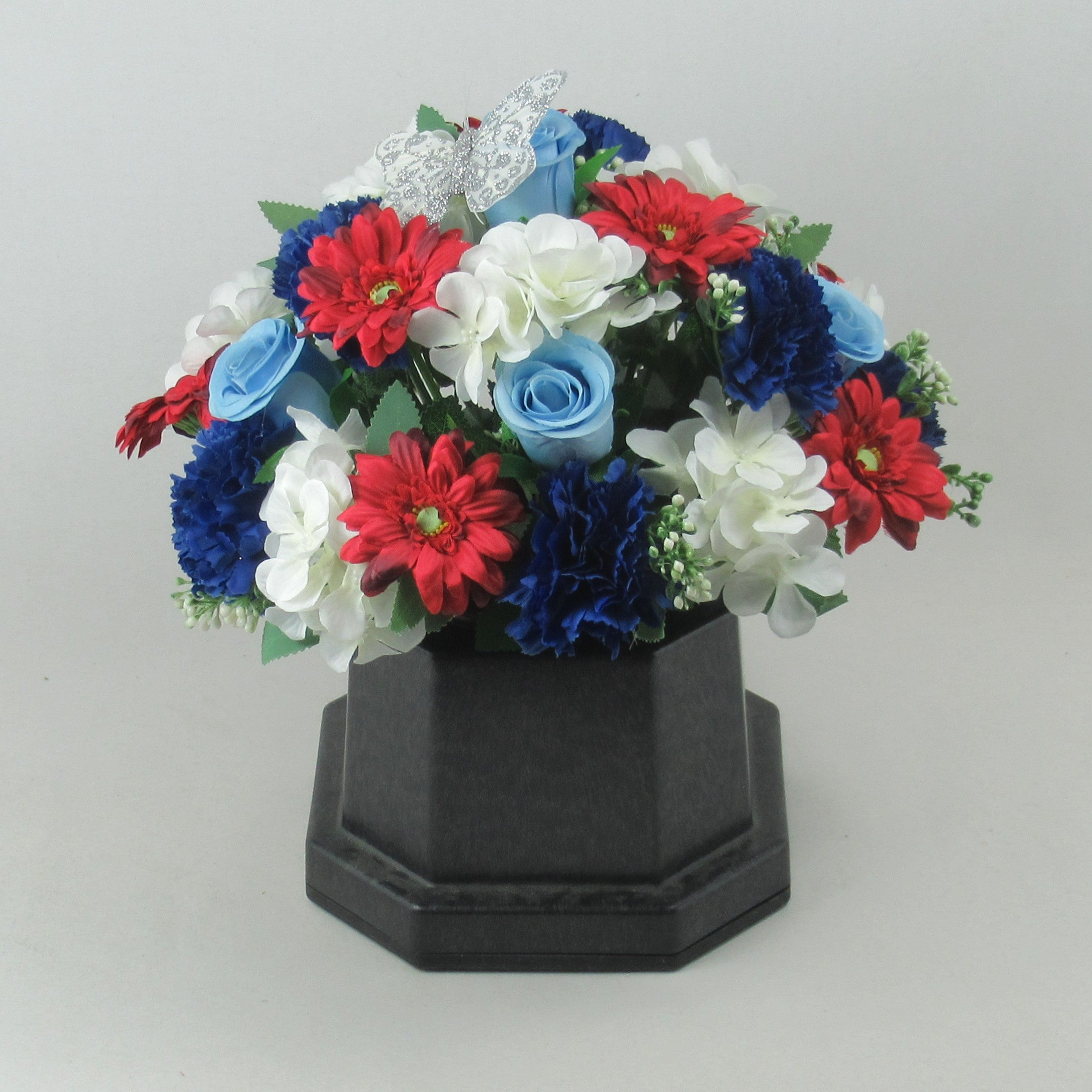 Artificial grave flower arrangement in dark vase with red, blue, and white blooms